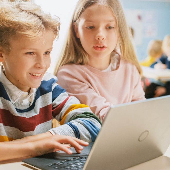 Brilliant Schoolgirl and Schoolboy Talk and Use Laptop to Program Software for Robotics Engineering Class. Elementary School Science Classroom with Children Working on Technology. STEM Education